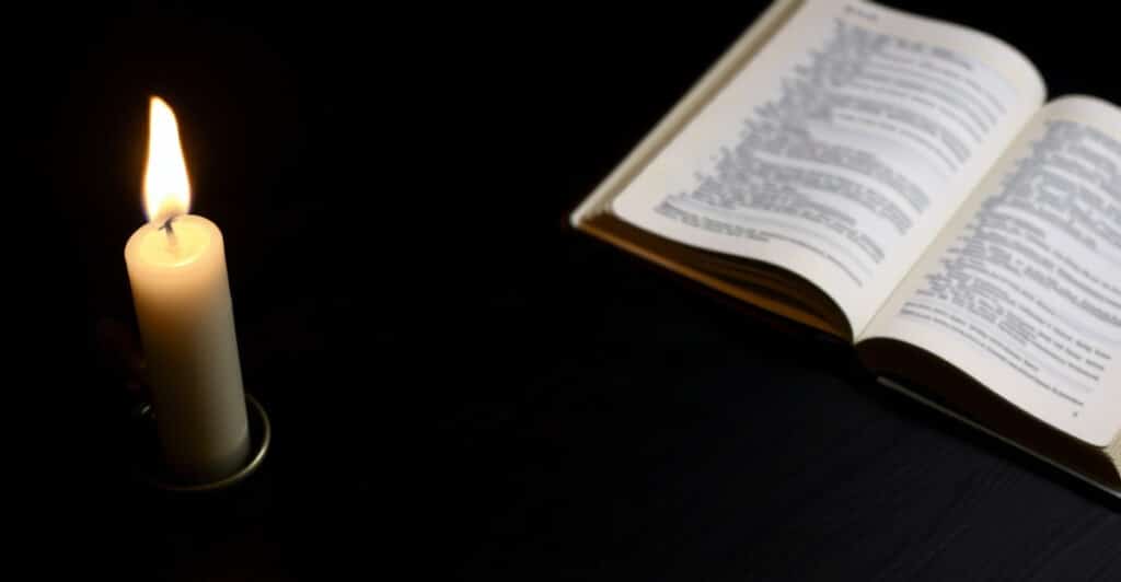 Una vela casi consumida junto a una Biblia abierta y un cuaderno cerrado de noche